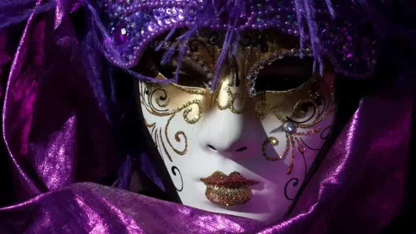 Close em uma luxuosa máscara de Carnaval veneziano nas cores roxo e dourado, com detalhes brilhantes e penas, representando a elegância das festividades italianas.