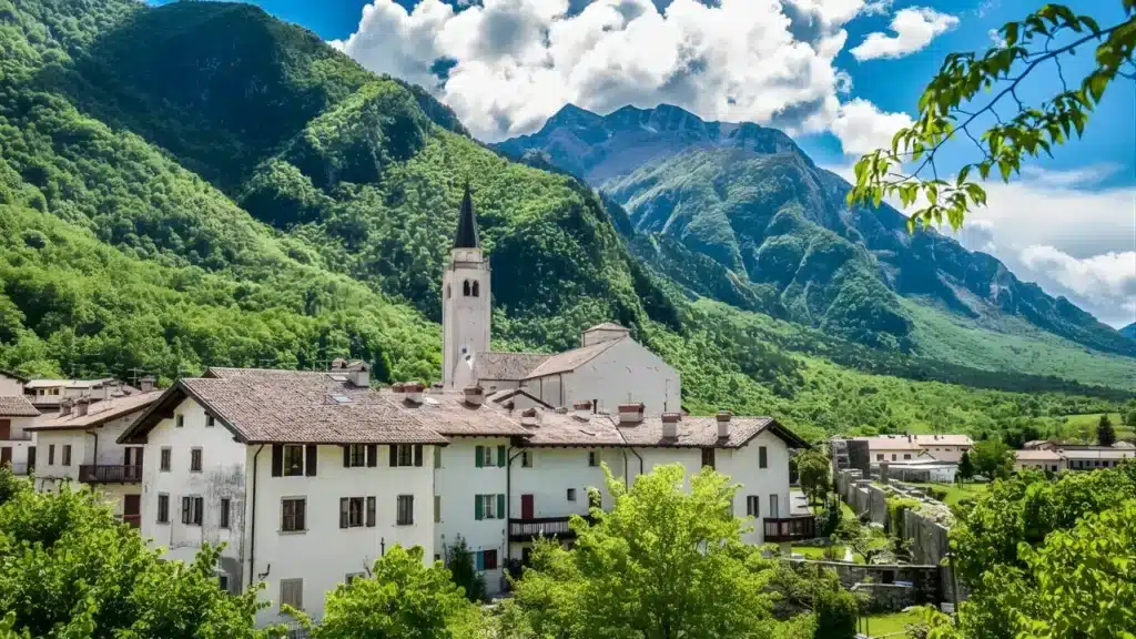Vilarejo medieval de Venzone com casas de pedra e torre de igreja aos pés de montanhas verdes nos Alpes italianos, região de Friuli